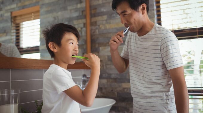 Father and son brushing teeth together in bathroom
